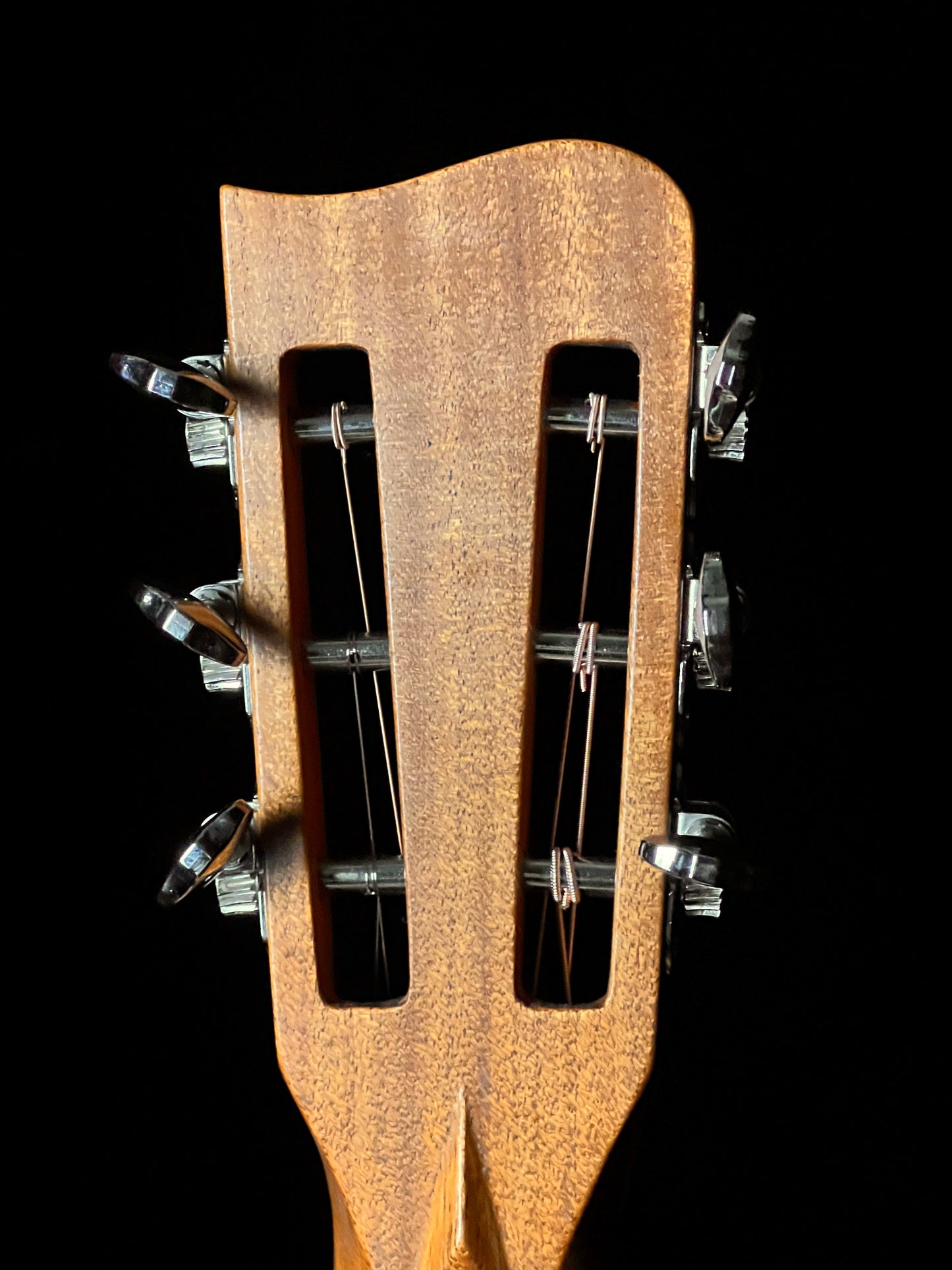 Close-up of a guitar's wooden headstock with tuning pegs on a black background