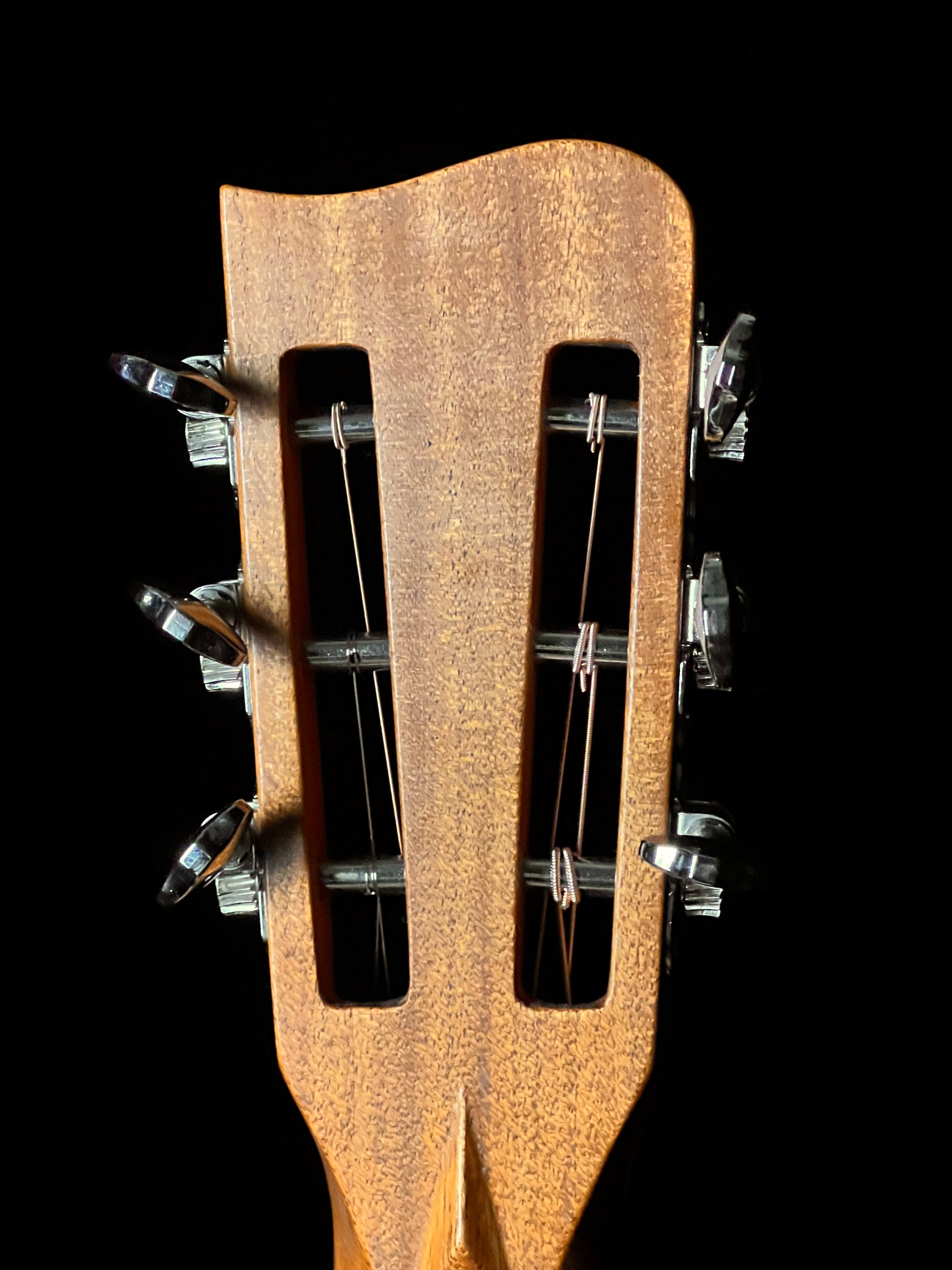 Close-up of a guitar's wooden headstock with tuning pegs on a black background